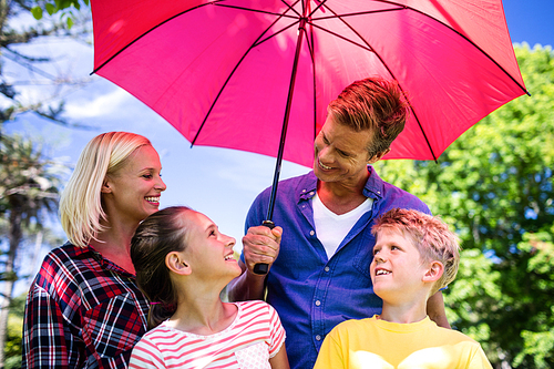 Happy family standing under pink umbrella in park