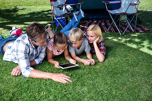Family lying on grass and using digital tablet at campsite