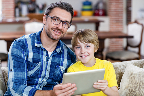 Portrait of father and son using digital tablet in living room at home