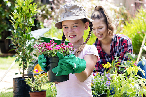 Portrait of girl standing in garden with flower pot while mother gardening in background