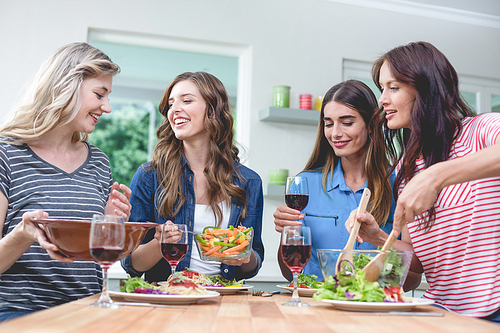 Friends holding glass of red wine while having meal at home