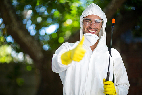 Portrait of man showing thumbs up while holding insecticide sprayer in lawn