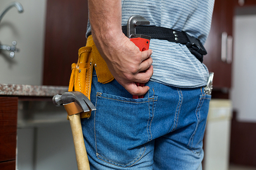 Rear view of man putting pipe wrench in pocket while standing at home