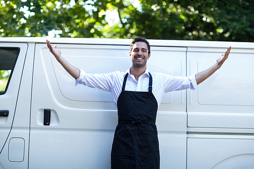 Portrait of confident delivery man with arms outstretched standing against van