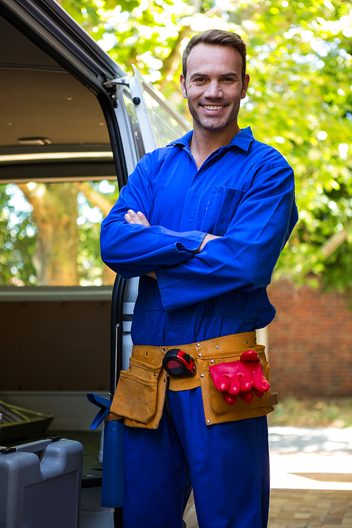 Portrait of mechanic with a tool belt around waist standing near a car