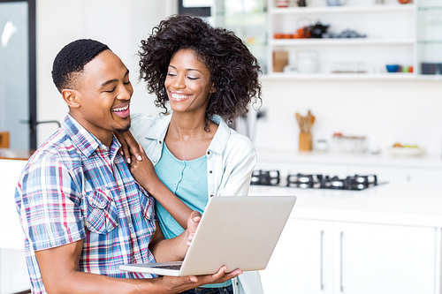 Happy young couple using laptop in kitchen at home