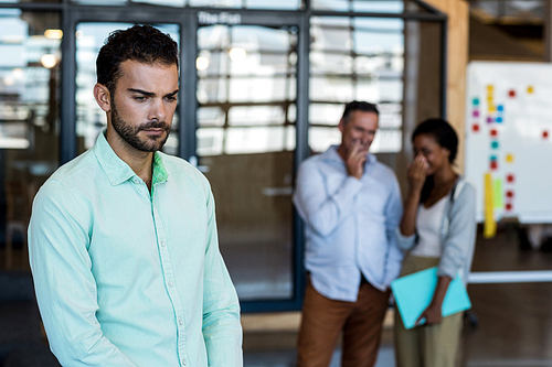 Depressed young man in the foreground while colleagues laughing standing in the background