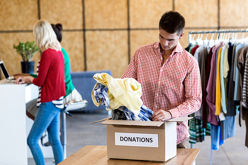 Young man sorting clothes from donation box while colleague standing in the background