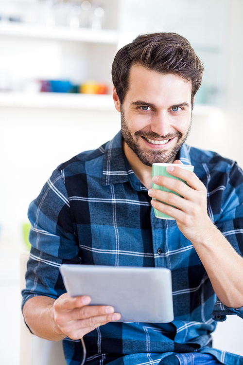 Happy man using digital tablet while having coffee in kitchen