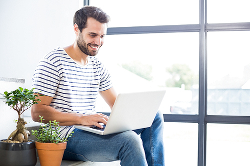 Happy man sitting on steps using laptop at home