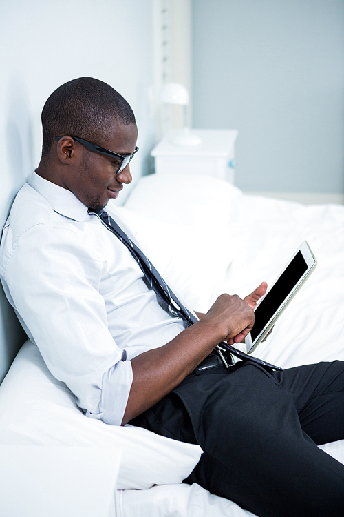 Young man using digital tablet on bed in bedroom