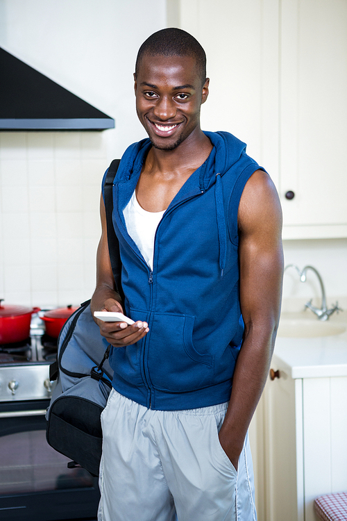 Man with gym bag holding a mobile phone in kitchen at home