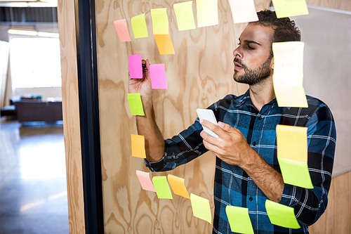 Man using mobile phone while writing on sticky notes in office