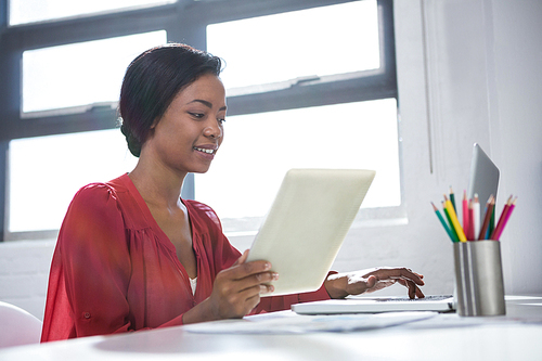 Woman using laptop and holding digital tablet in office