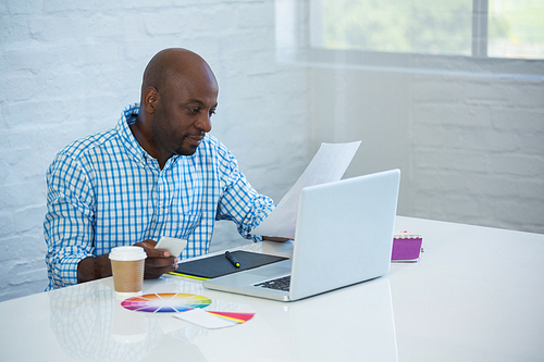 Graphic designer reading a document with laptop on table in office