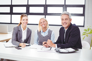 Portrait of happy business people sitting with client at desk in office
