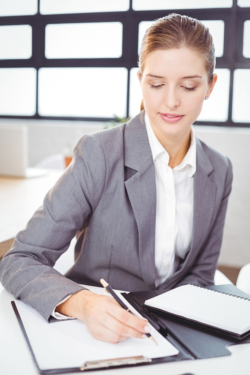 Close-up of beautiful businesswoman writing on notepad at desk in office
