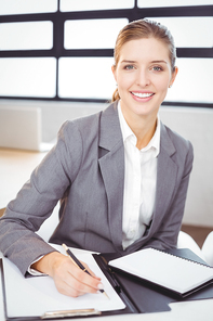 Portrait of beautiful young businesswoman with documents sitting at desk in office