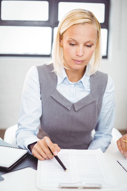 Businesswoman reading documents while sitting at desk in office