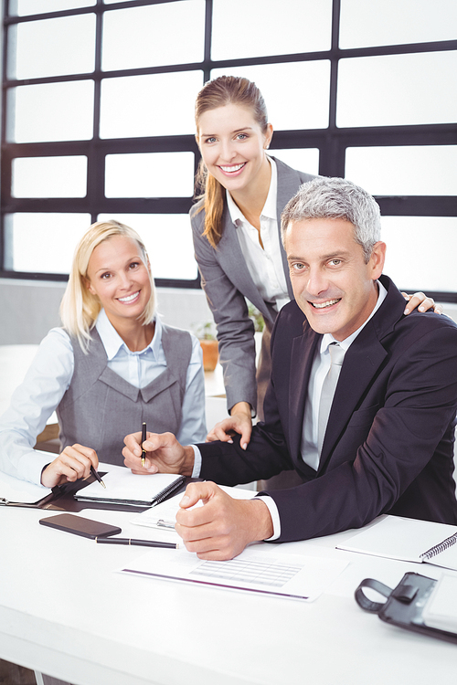 Portrait of happy business people with client at desk in meeting room