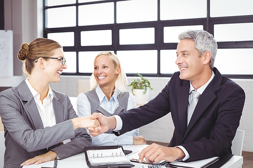 Happy business people handshaking during meeting at desk in office