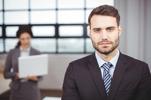 Close-up portrait of confident young businessman while colleague in background at office