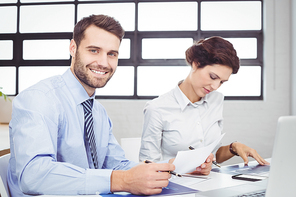 Portrait of happy businessman with document while female colleague sitting beside