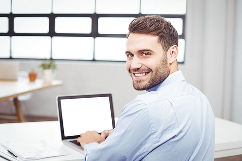 Close-up portrait of happy businessman using laptop at desk in office