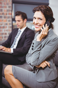 Happy businesswoman using mobile phone while colleague working in background
