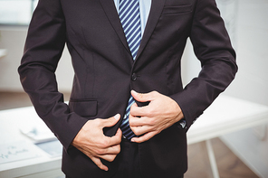 Midsection of businessman adjusting suit while standing in office