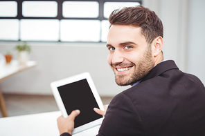 Close-up portrait of happy businessman using digital tablet while sitting at desk in office