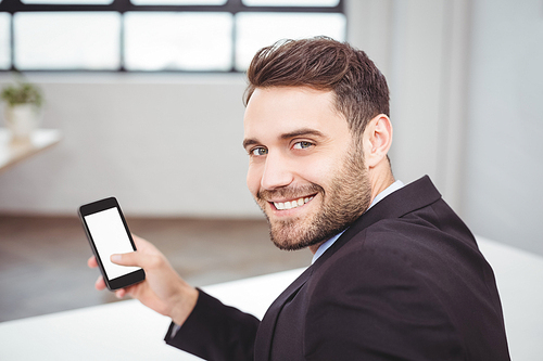 Close-up portrait of happy businessman using mobile phone while sitting at desk in office