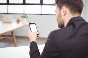 Rear view of businessman using smartphone while sitting at desk in office