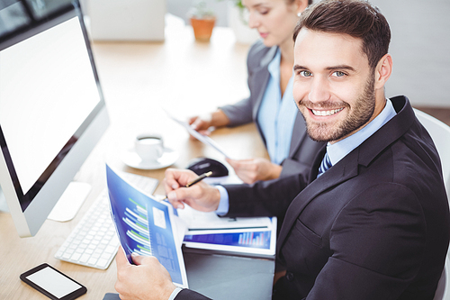 Portrait of happy businessman holding graph while sitting at computer desk