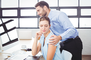 Businessman harassing female colleague at computer desk in office