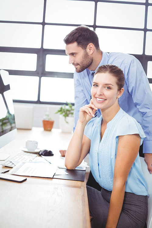 Portrait of businesswoman smiling while sitting by colleague at computer desk in office