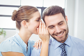 Close-up of happy businesswoman whispering to male colleague in office