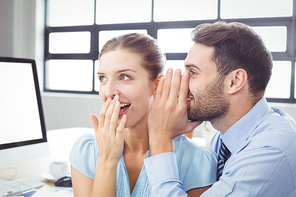 Close-up of happy businessman whispering to female colleague in office