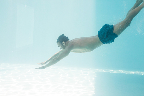 Side view of shirtless man swimming under swimming pool