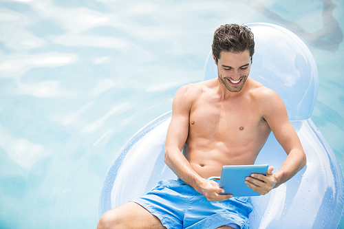 Happy shirtless man using digital tablet on swim ring at swimming pool