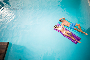 High angle view of young couple relaxing on inflatable raft at swimming pool