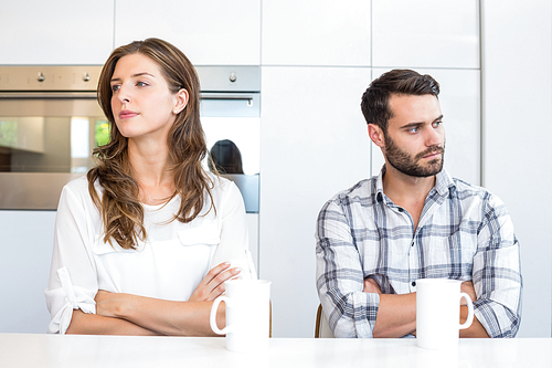 Upset couple with arms crossed sitting by table at home