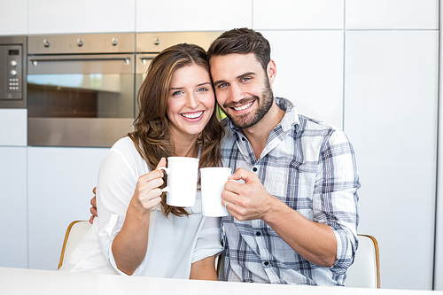 Portrait of happy couple drinking coffee by table at home