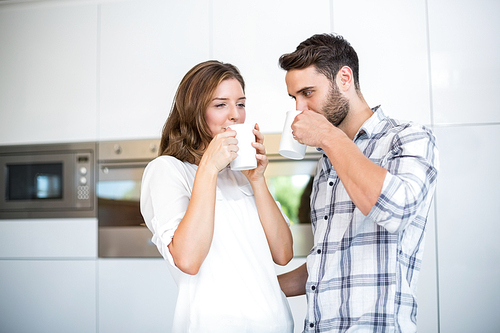 Couple drinking coffee while standing in kitchen at home