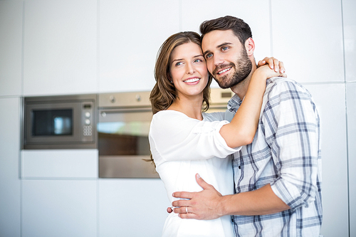 Happy couple looking away while embracing in kitchen at home