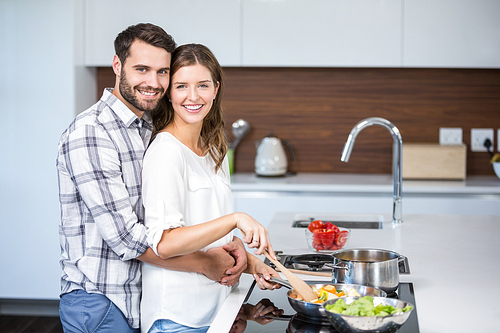 Portrait of man embracing woman while preparing food at kitchen counter