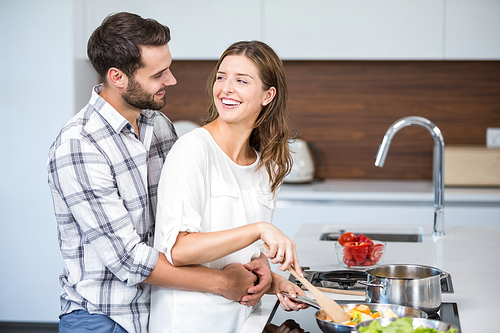 Happy man embracing woman while cooking food at kitchen counter