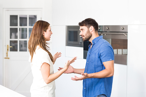 Couple arguing while standing in kitchen at home