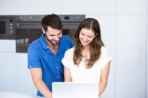 Happy couple using laptop in kitchen at home