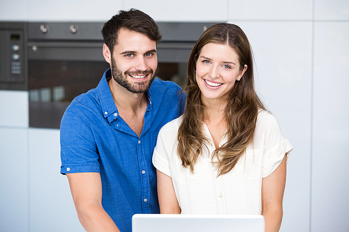 Portrait of happy couple with laptop standing at home